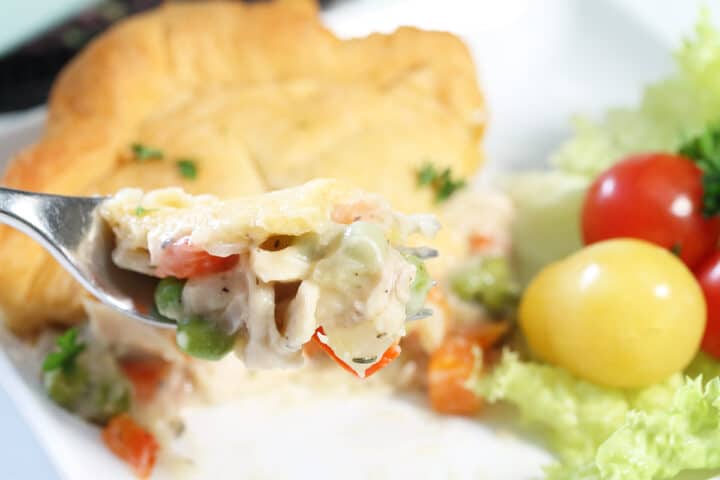 Bite of pot pie on fork over dinner plate.