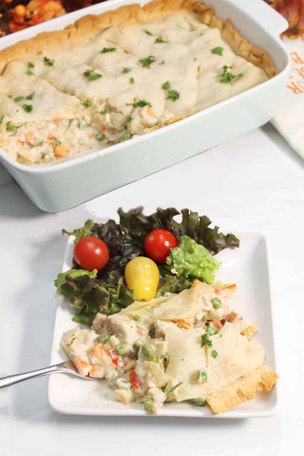 Serving of turkey pot pie on white plate with casserole in back.