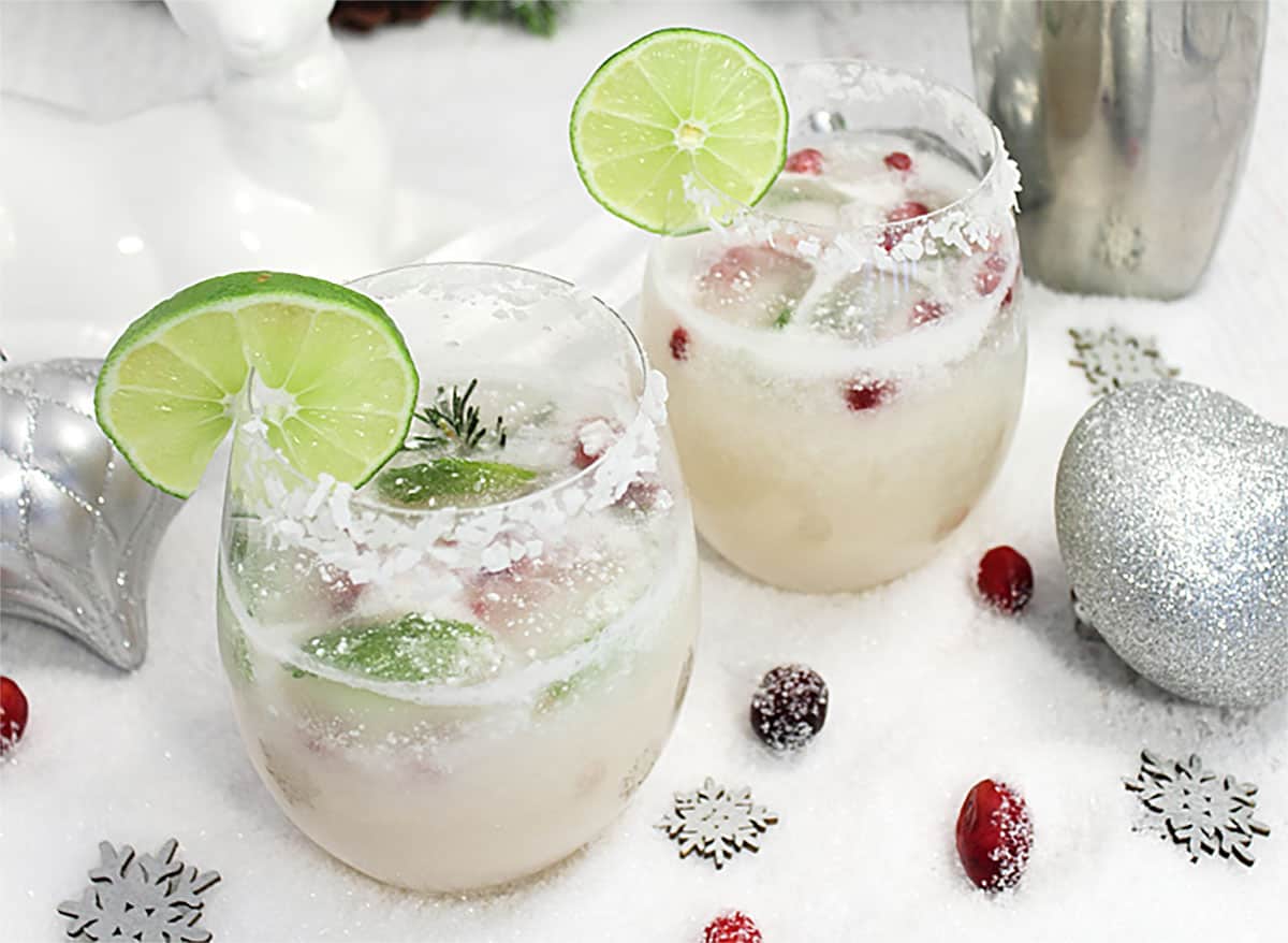 Cocktails on white table with sugared cranberries and ornaments scattered around.