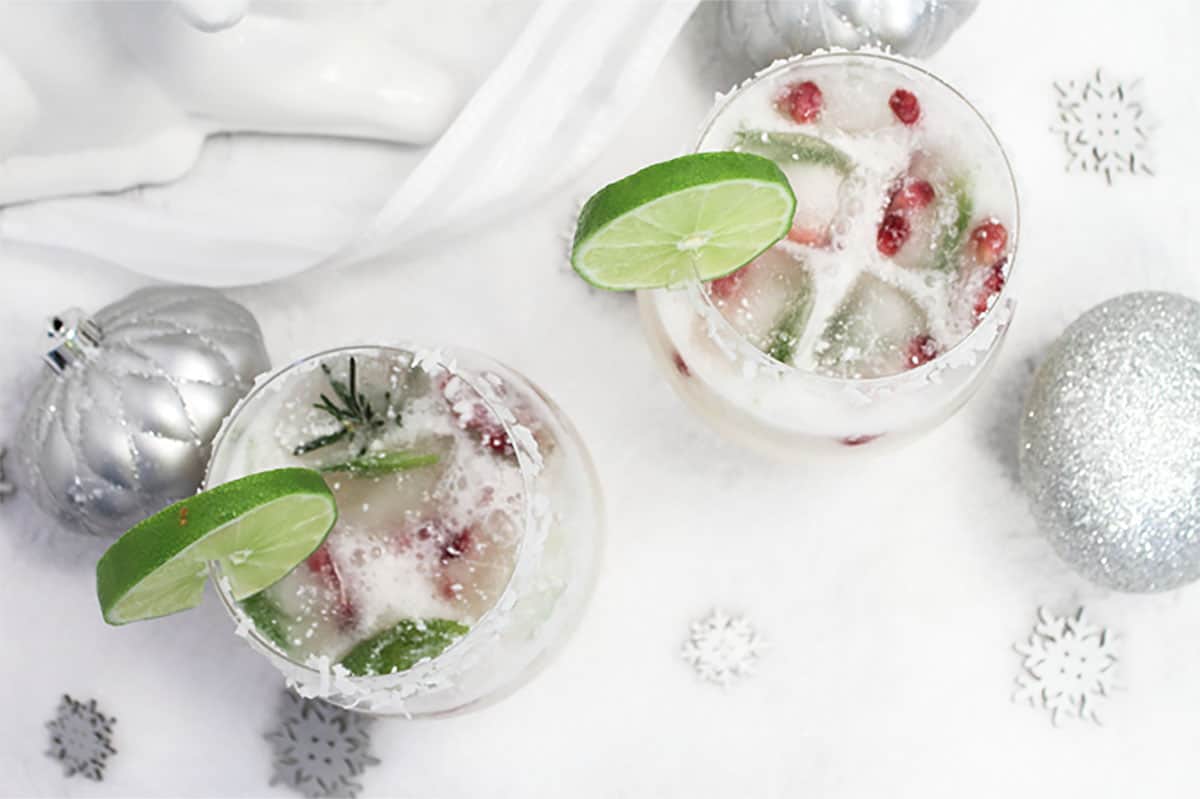 Overhead of holiday margaritas with pomegranate arils and slice of lime.