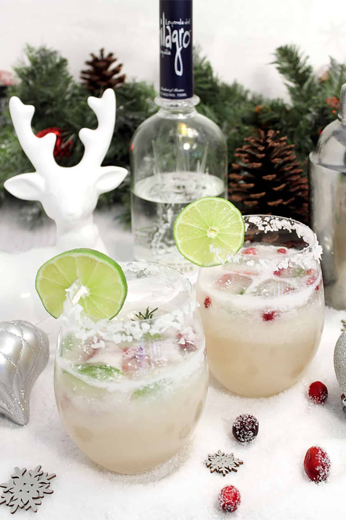 Two margaritas with lime wedge on white table with deer in background.