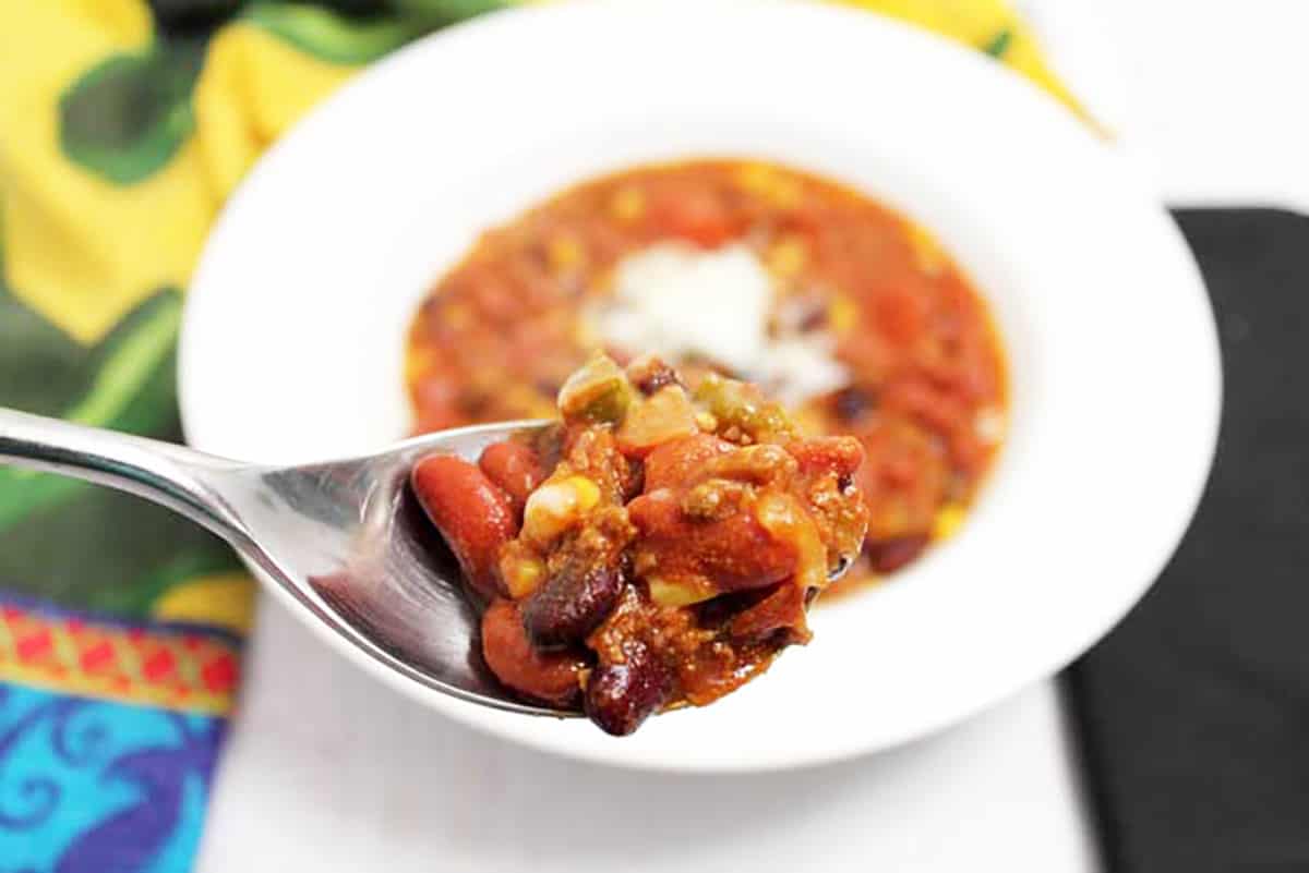 Closeup of bite of chili on spoon showing beans and seasoned beef in broth.