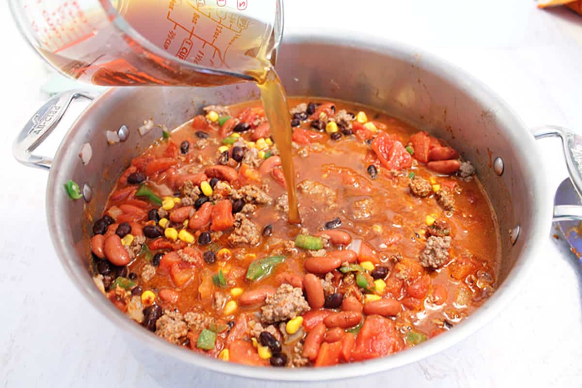 Pouring beef stock into chili mixture in large stock pot.