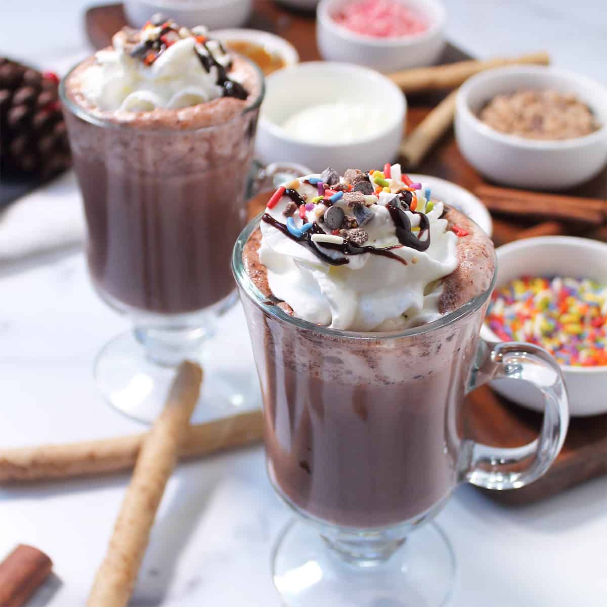 Two mugs of spiked hog chocolate beside hot chocolate bar.