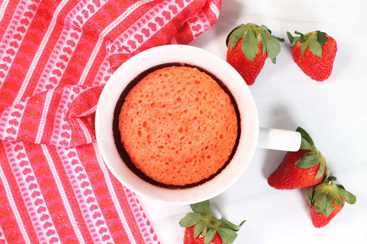 Baked Strawberry Mug Cake in white mug with strawberries around.