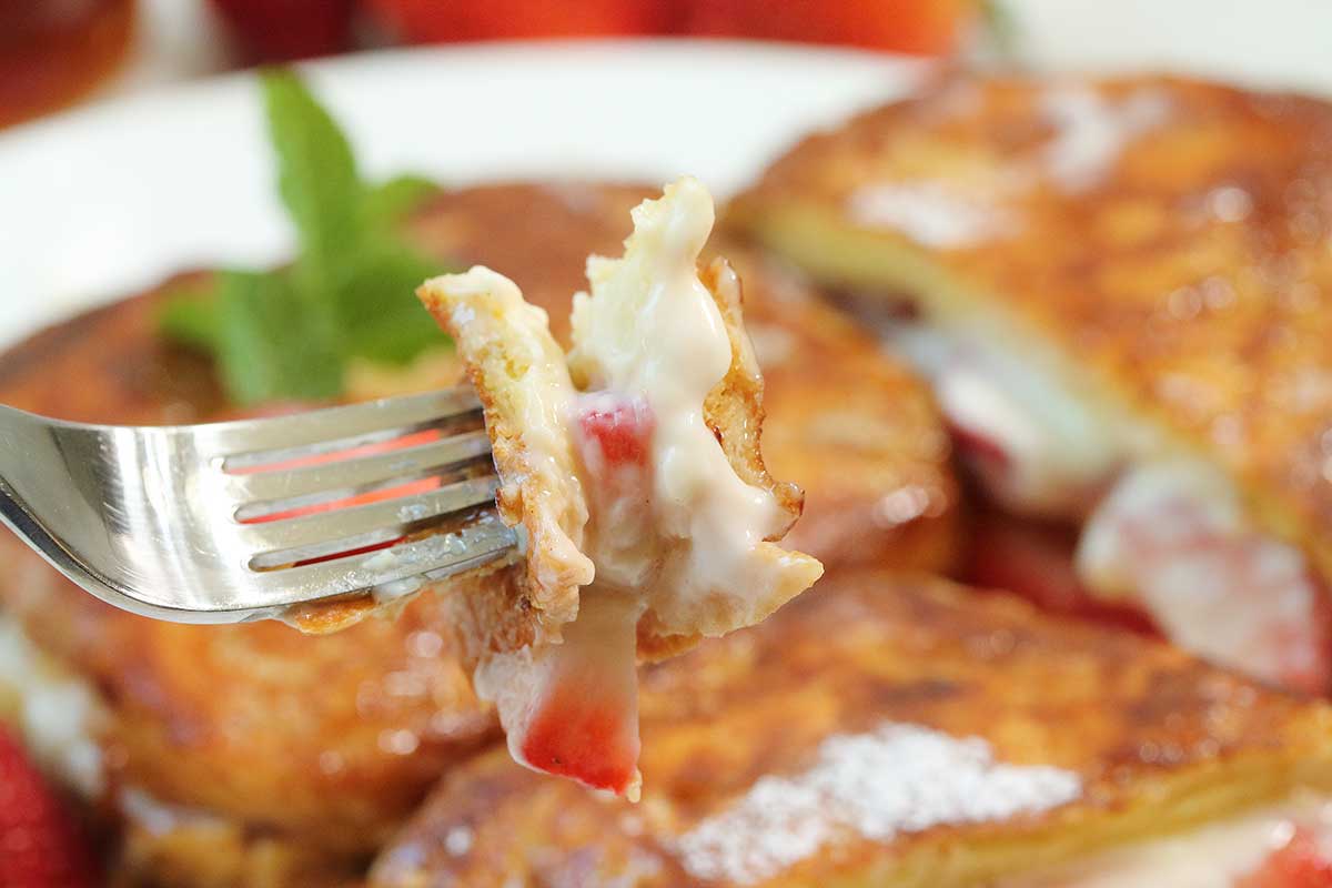 Bite of stuffed French toast with strawberries on fork.