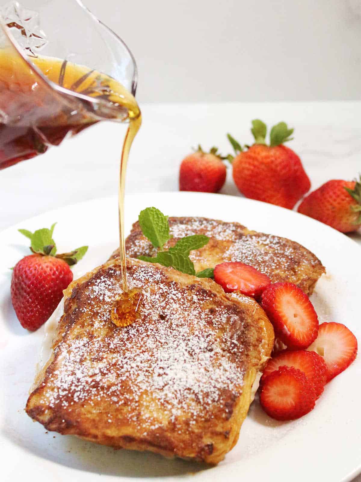 Pouring maple syrup over plate of strawberry stuffed French toast.