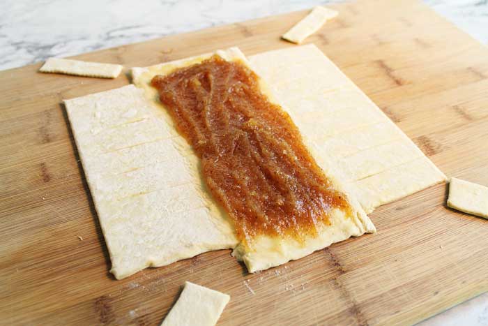 Putting almond filling on pastry on wooden cutting board.