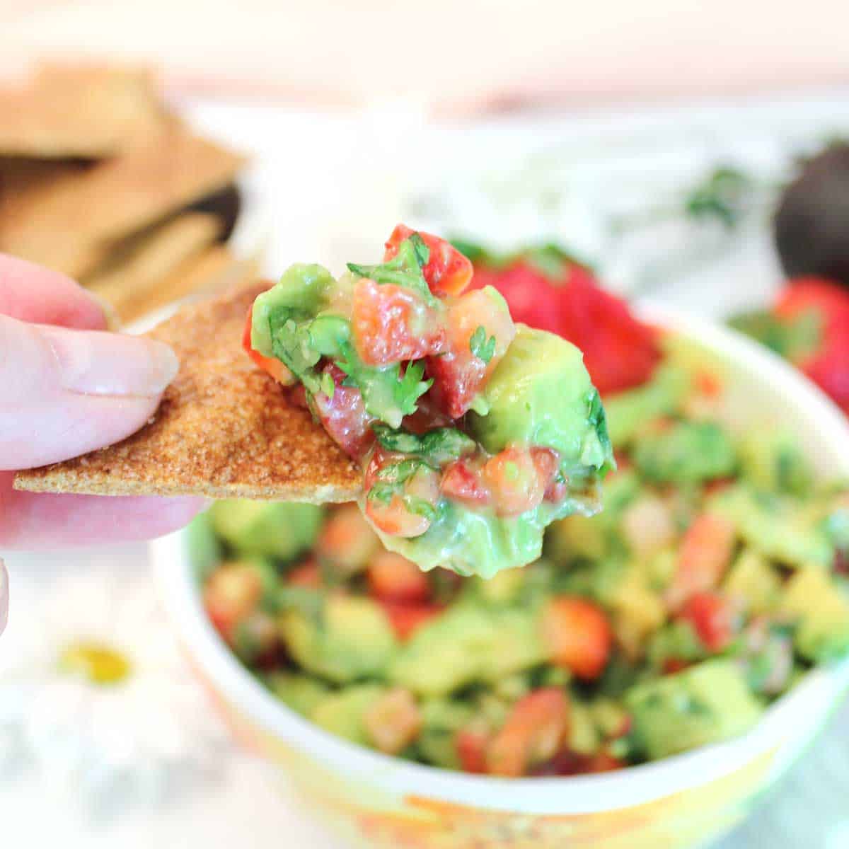 Holding a tortilla chip with avocado salsa on it.