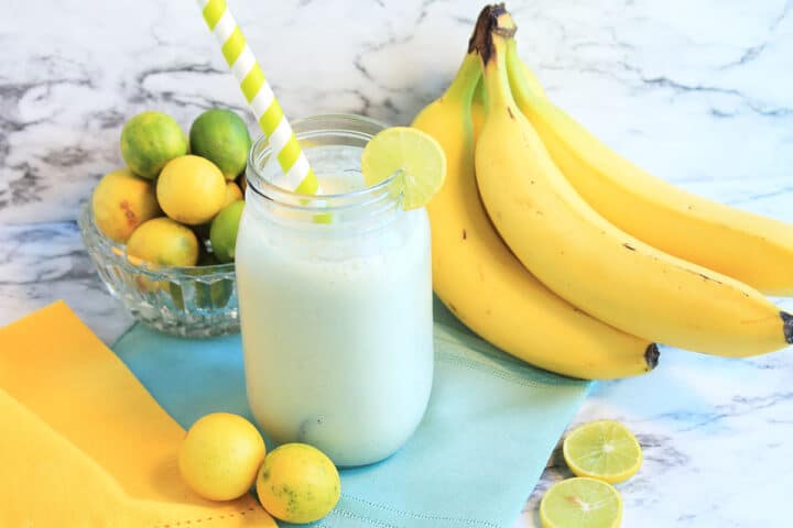 Lime Smoothie sitting on table with yellow napkin, bananas and key limes.