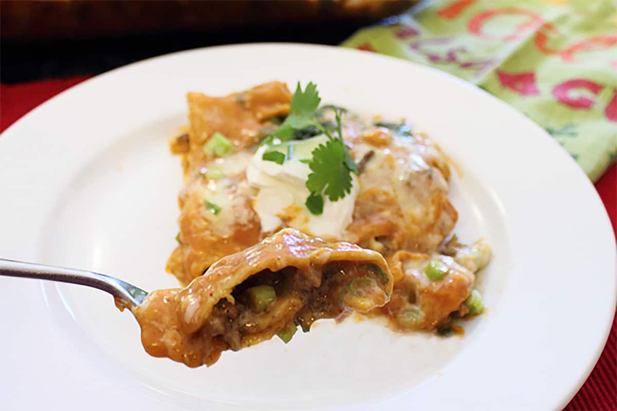 Taking a bite of creamy beef enchiladas from serving on white plate.
