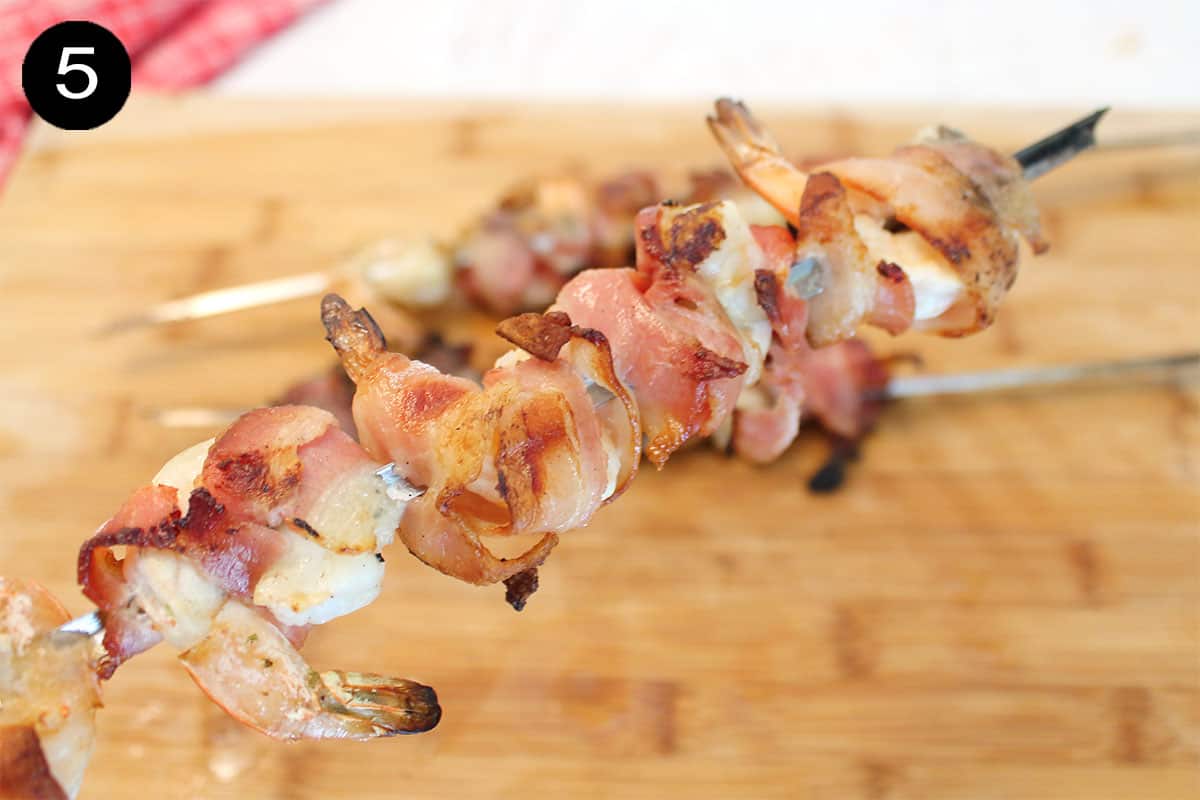 Holding skewer of grilled bacon wrapped shrimp.