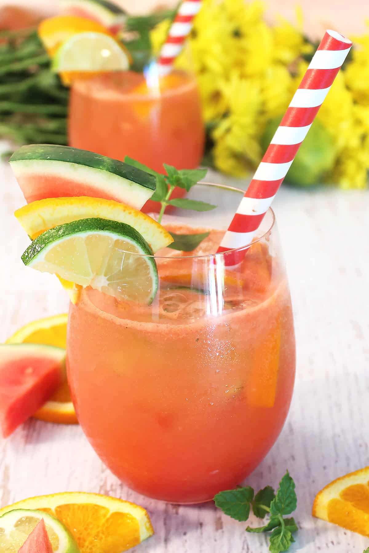 Closeup of Watermelon Sangria with red striped straw and garnished of lime, orange and watermelon on white table.
