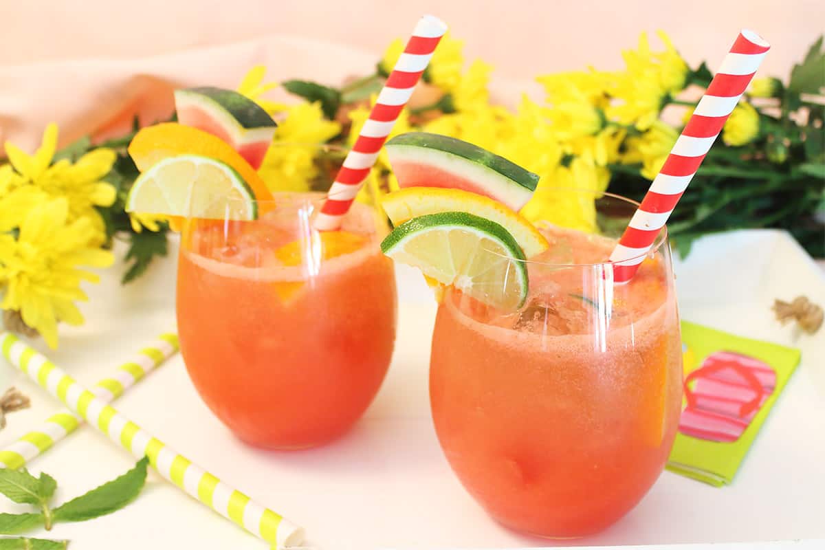 Summer sangria with red striped straws on white wooden try with yellow flowers in back.