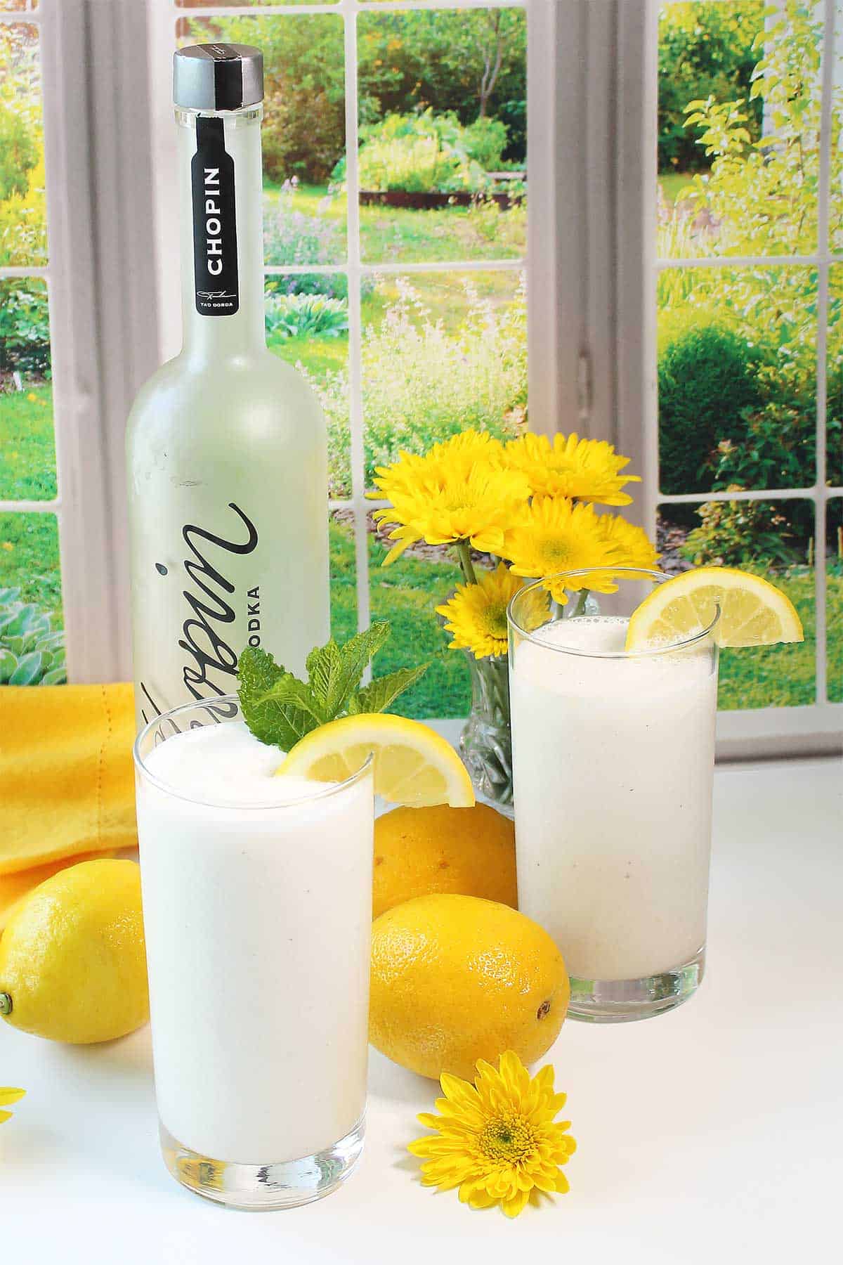 Two frosted lemonades in glasses with lemon and mint garnish.