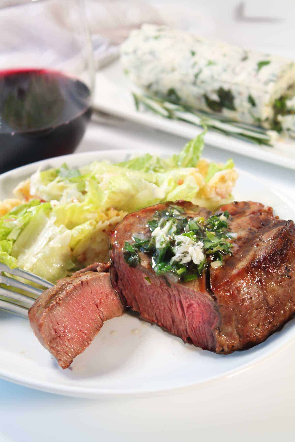 Bite of steak on fork on dinner plate.