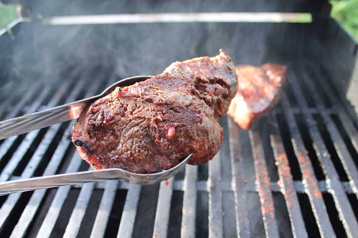 Holding a seared steak above the hot grill.