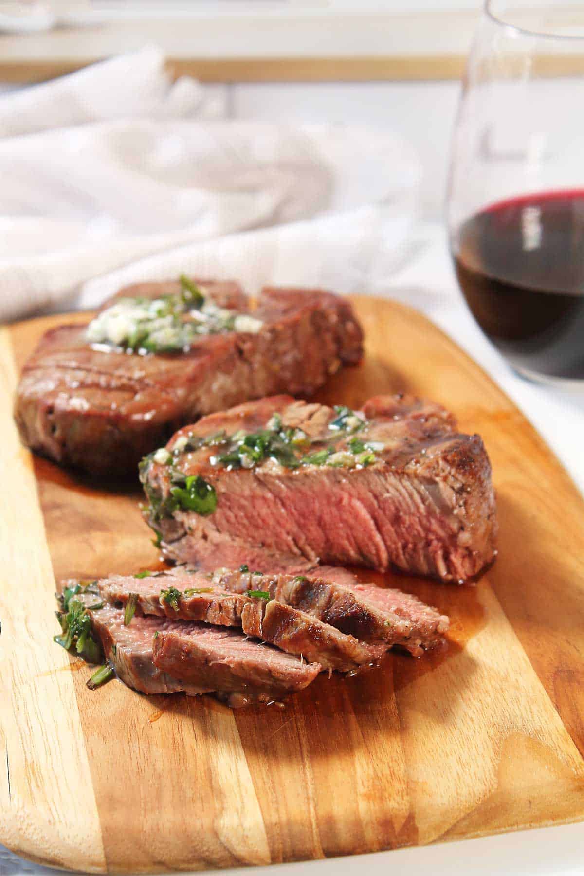 Grilled filet mignon sliced on cutting board and topped with herb garlic butter.