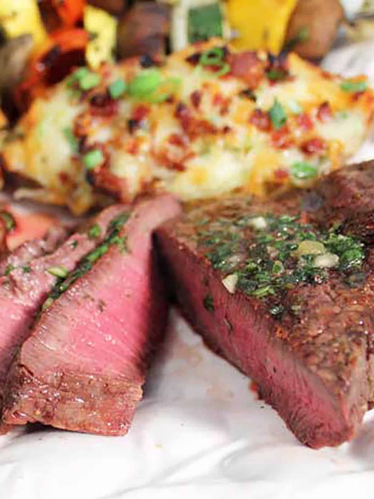 Medium rare steak sliced with baked potato in back.