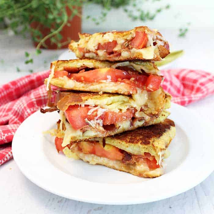 Stacked sandwiches on white plate with checkered towel in background.