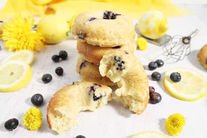 Baled Blueberry Doughnuts stacked with one cut in half and surrounded by lemons and blueberries.