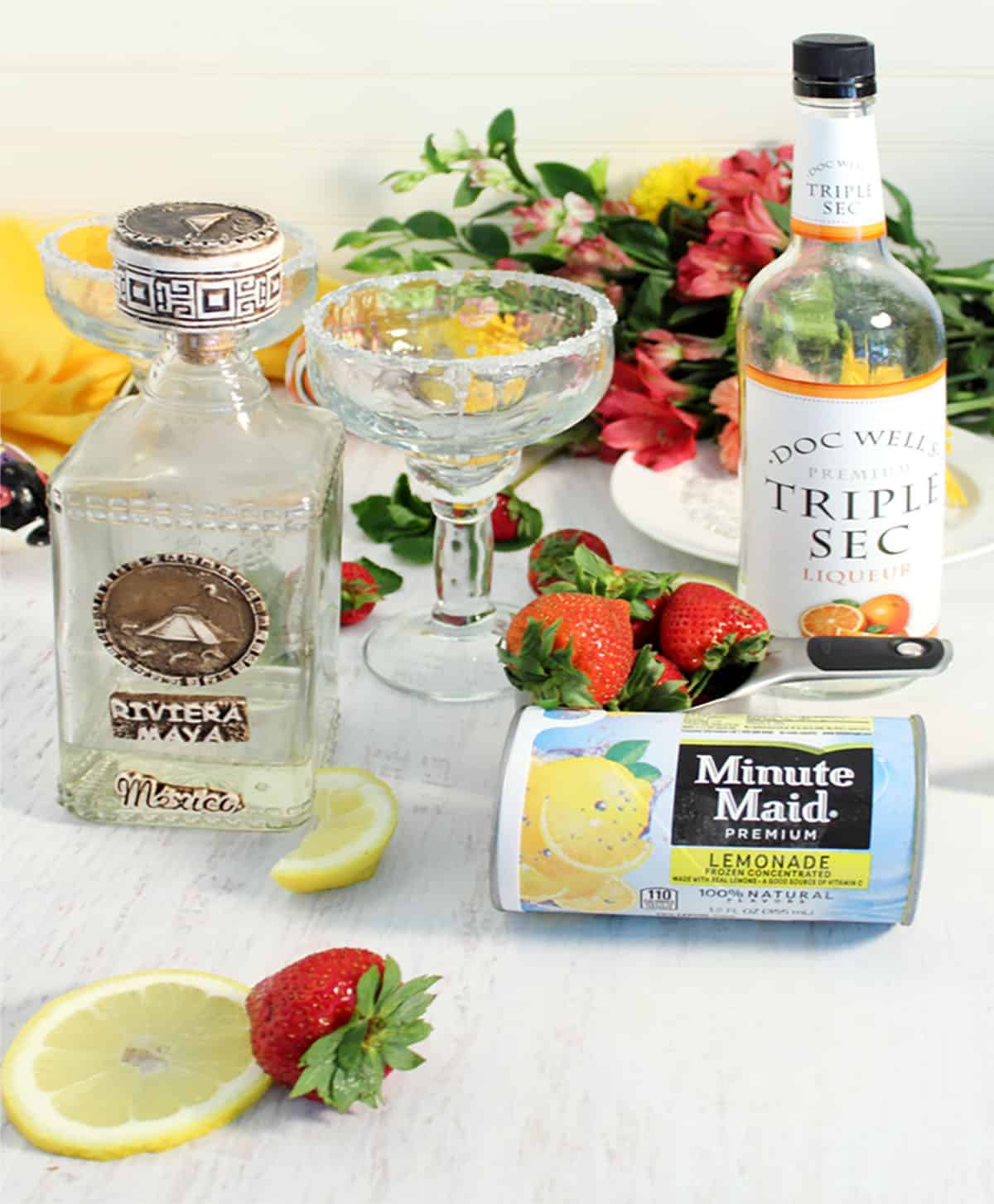 Ingredients for margarita on white table with flowers in background.