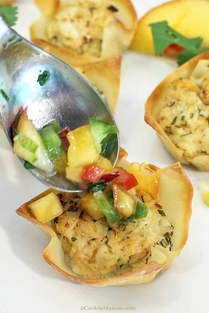 Goat Cheese Crab Wonton Cups with nectarine Salsa adding salsa | 2 Cookin Mamas Goat Cheese Crab Wonton Cups are an easy, tasty appetizer for entertaining. Creamy goat cheese is topped with a mini crab cake and baked in a wonton cup for the perfect handheld appetizer that is sure to please all seafood lovers. Top them with a little nectarine salsa for an extra special kick. #appetizer #crabcakes #goatcheese #fall #recipe #wontoncups #TheFreshMarket TFMCrabBash #AD
