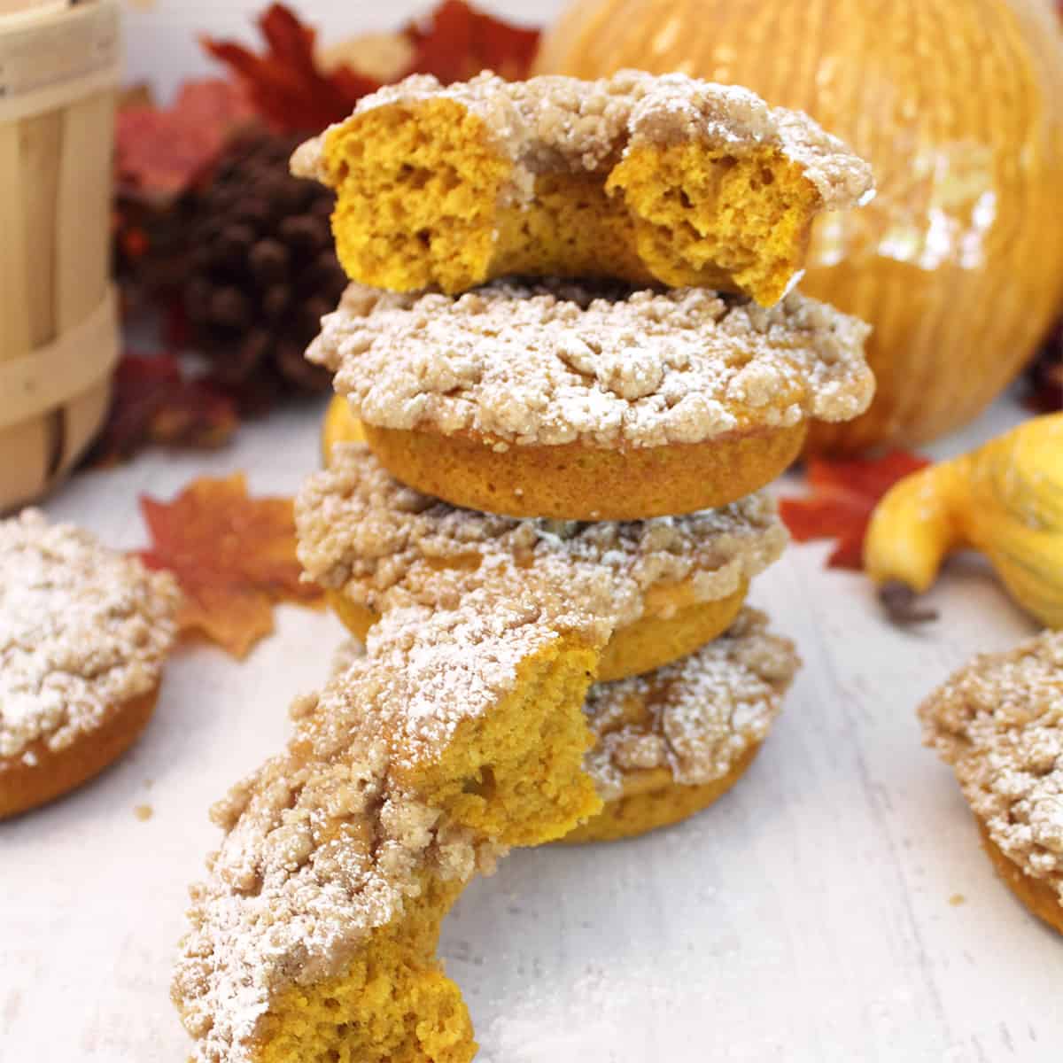 Stack of crumb topped donuts on white table with half a donut in front.