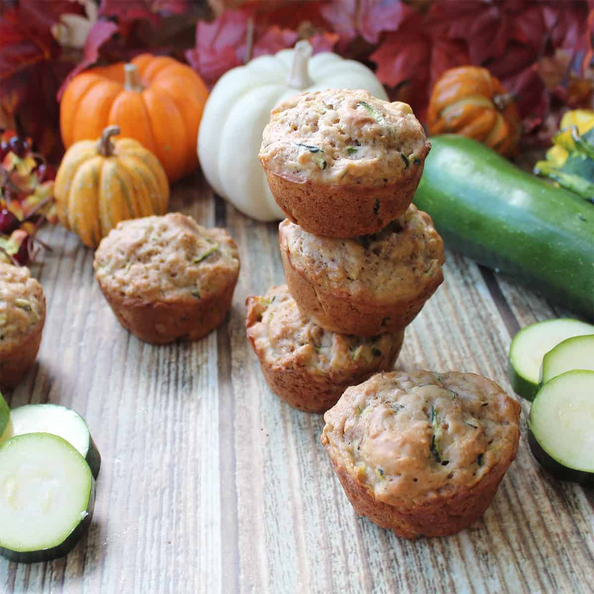 Stacked muffins with zucchini and fall foliage in back.
