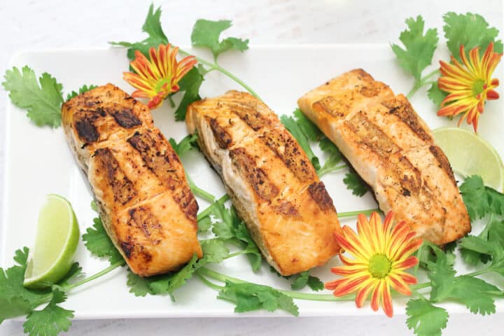 Three servings of salmon on white platter with lime wedge.
