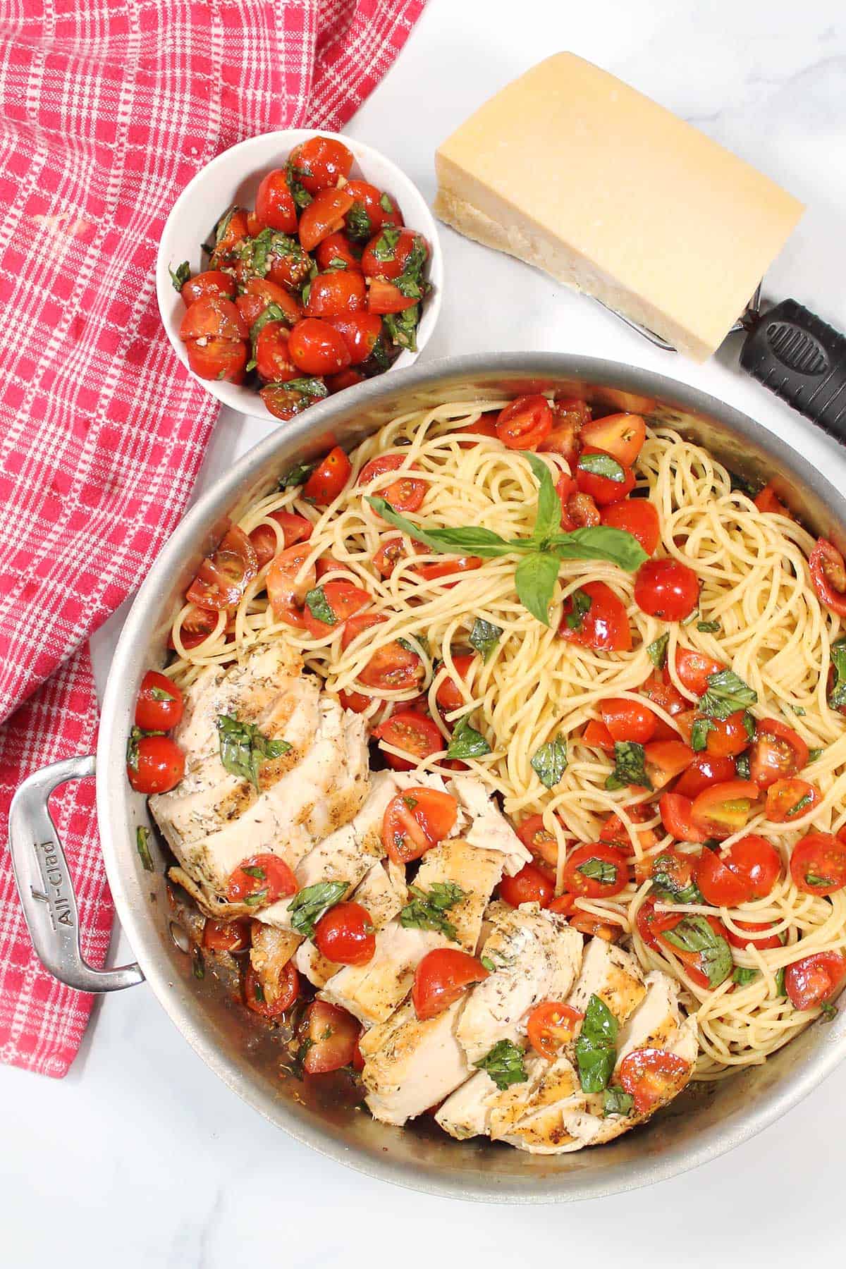 Finished bruschetta chicken pasta in skillet with Parmesan cheese and extra bruschetta next to it.