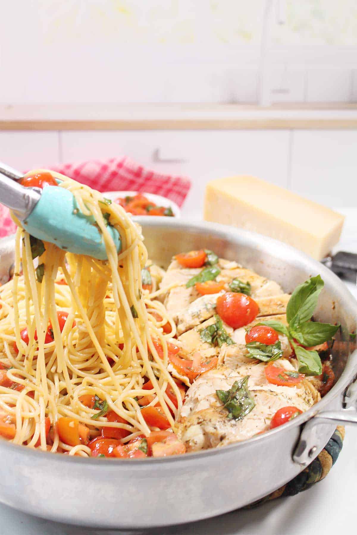 Lifting a serving of pasta with bruschetta sauce with tongs.