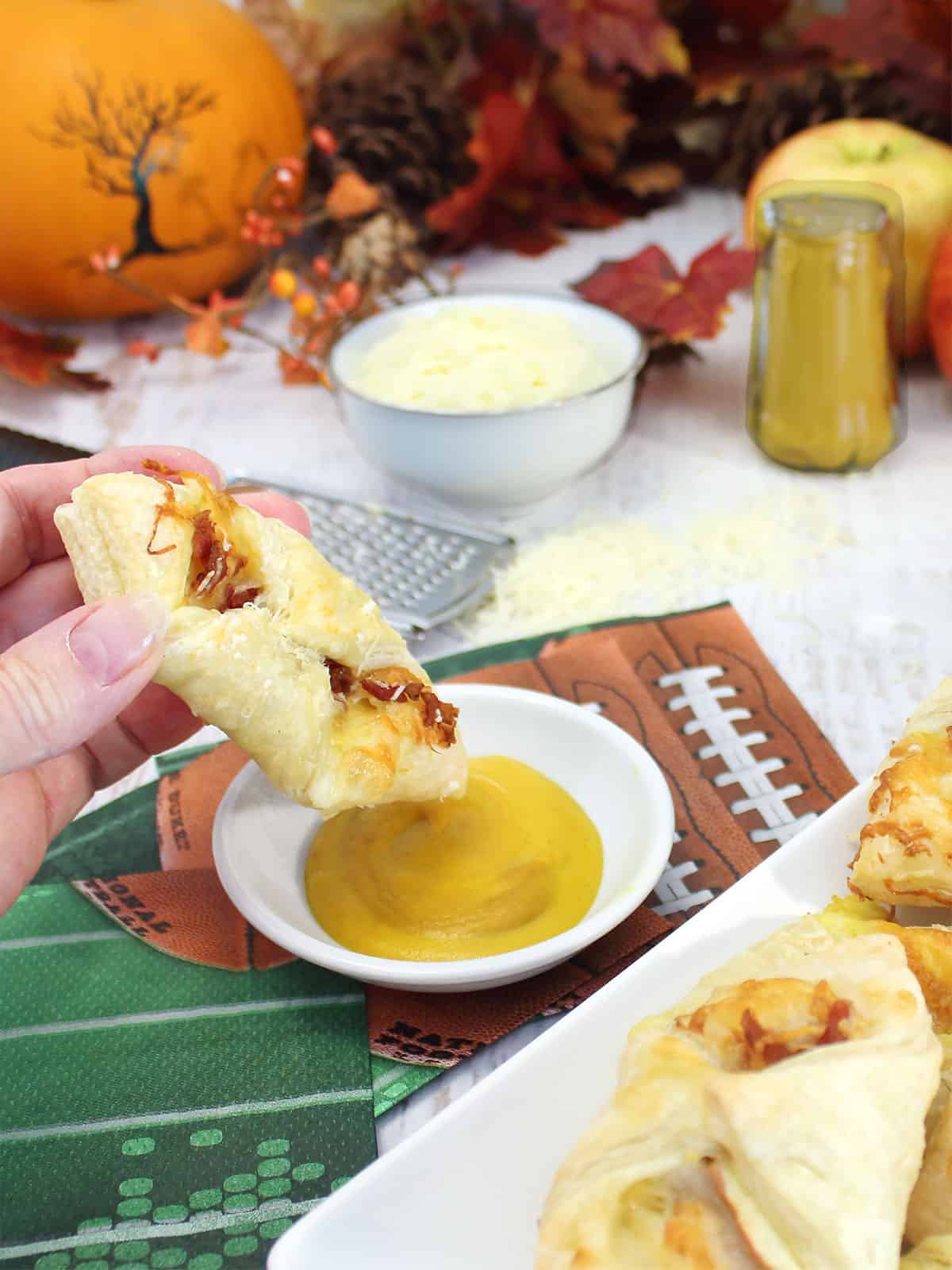 Dipping apple bacon cheese puff pastry bites in mustard.