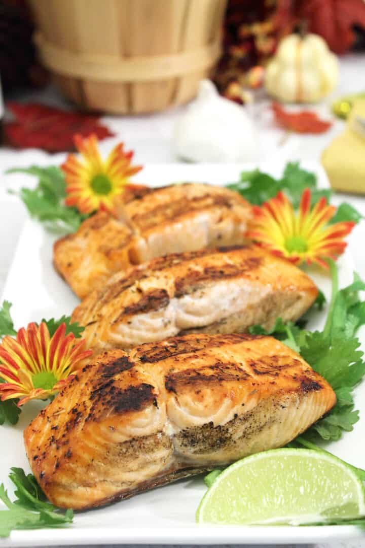 Grilled salmon on white platter with lime wedge and flowers.