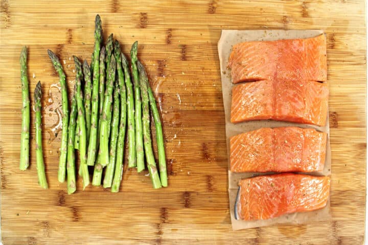 Seasoned salmon on wooden cutting board with asparagus.