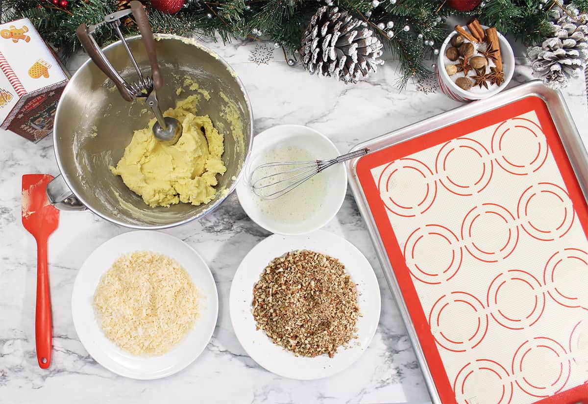 Assembly line of chopped nuts, egg whites and cookie dough on marble table.