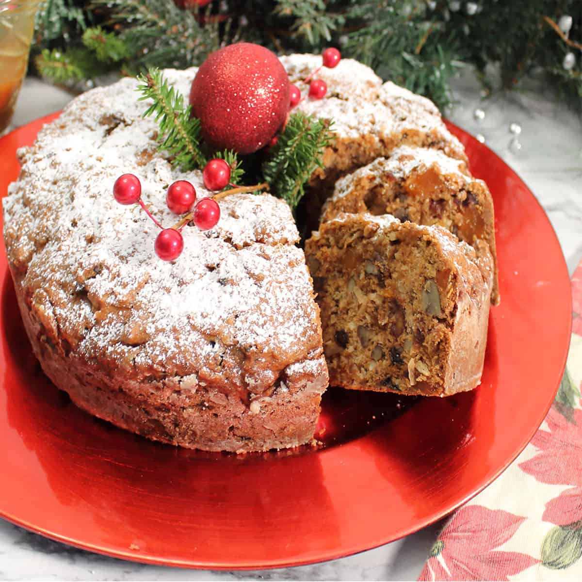 Decorated sliced fruitcake on red platter.