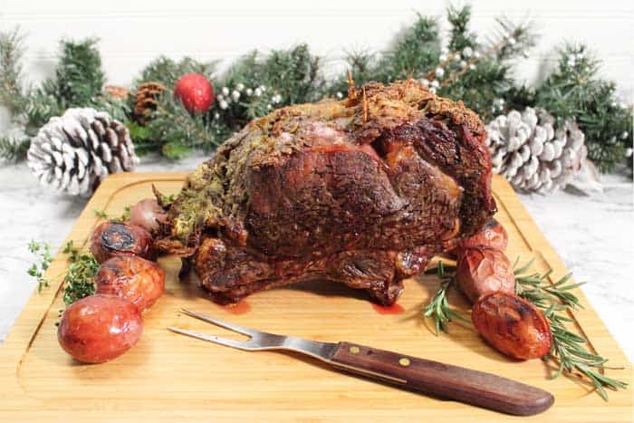 Perfectly cooked prime rib roast on cutting board with greenery in background.