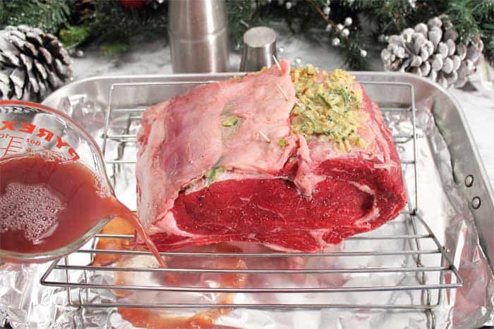 Securing flap over garlic butter and adding red wine to bottom of roasting pan.