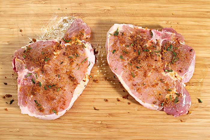 Seasoned pork chops on wooden cutting board.