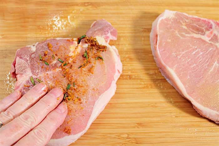 Patting on seasoning on chops on wooden cutting board.