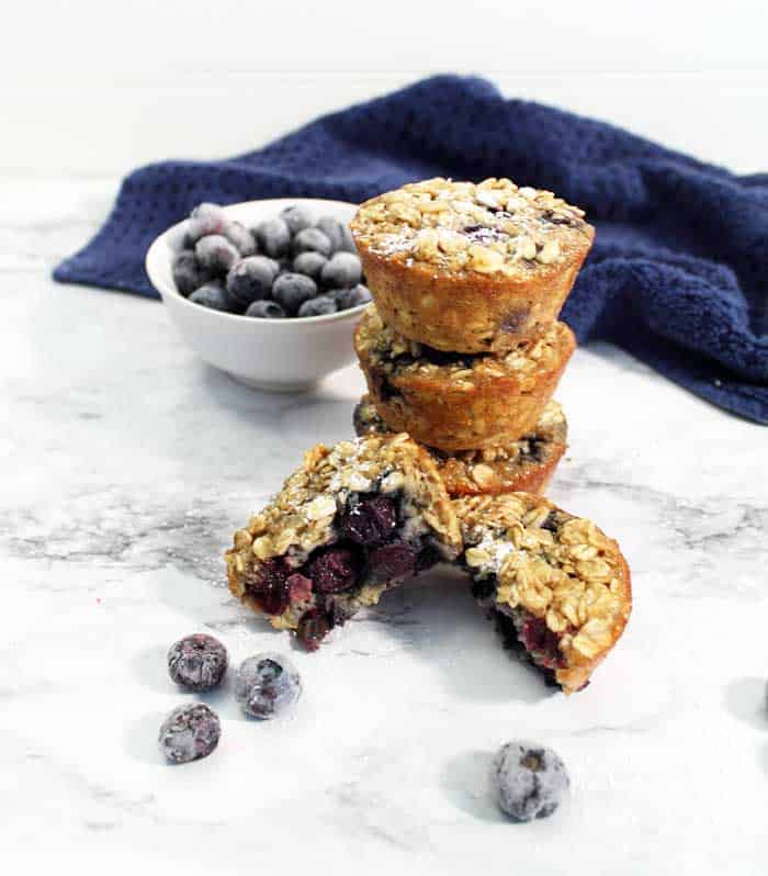 oatmeal muffins stacked on a marble background with the front muffins broken in half.
