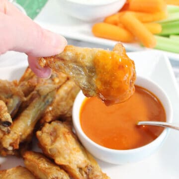 Closeup of air fried wing dipped in buffalo sauce.