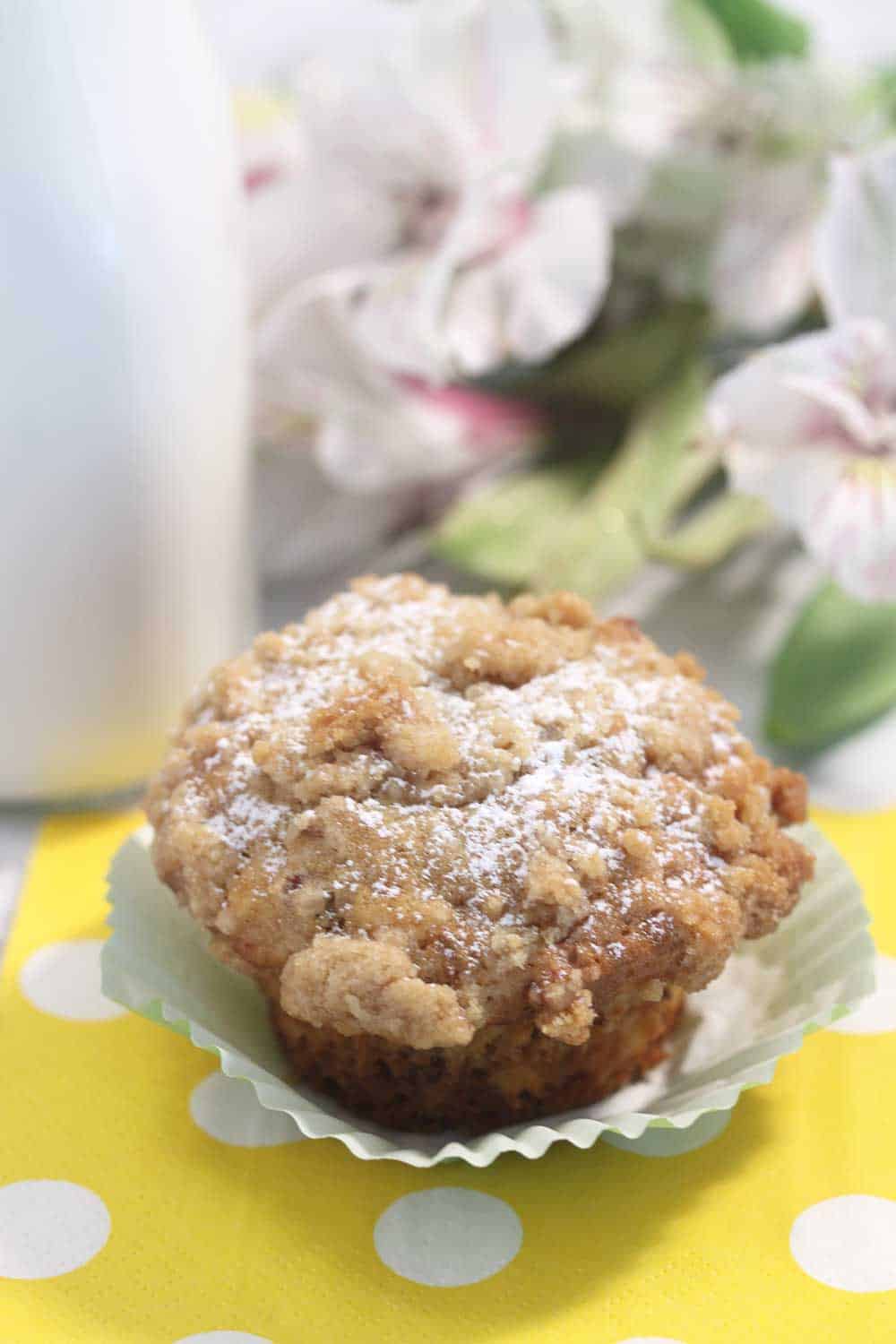 Single muffin with crumbs and powdered sugar on top with milk jug in background.