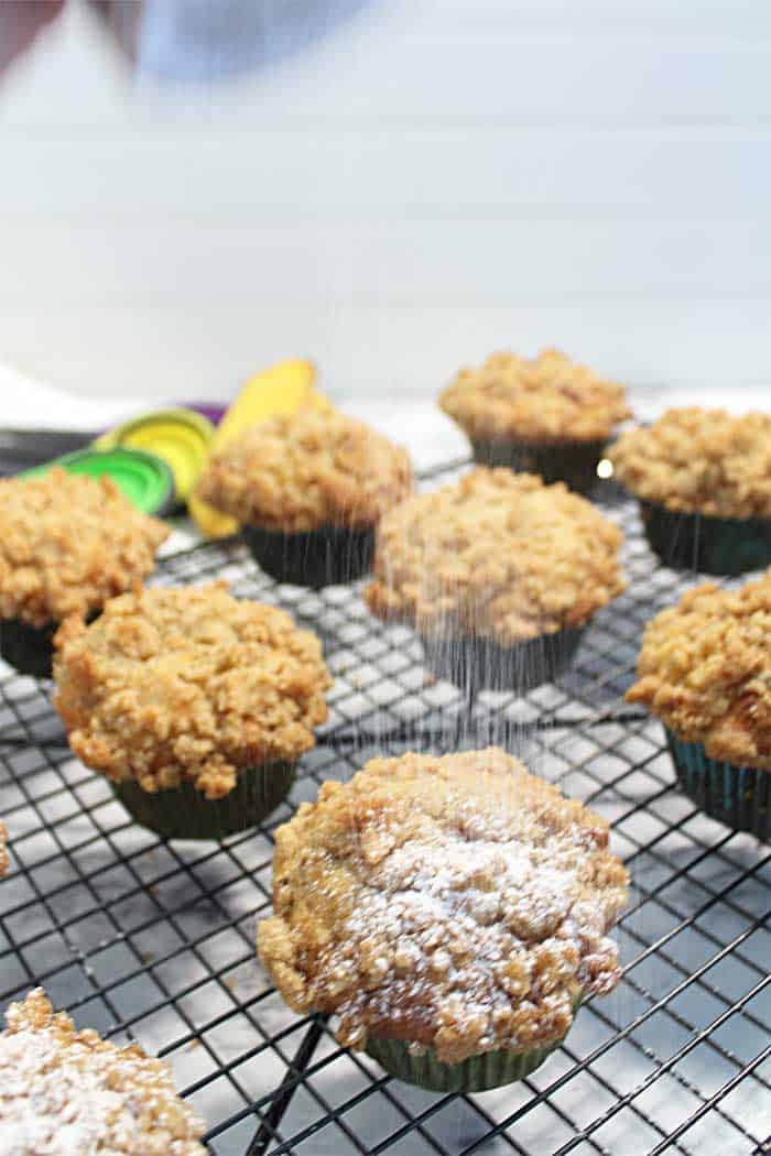 Sprinkling powdered sugar on muffins on wire rack.