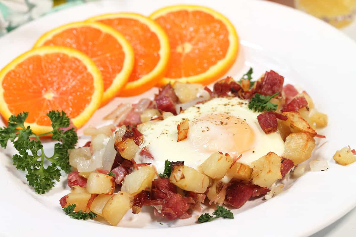 Plate of hash and egg with orange slices and garnished with parsley.