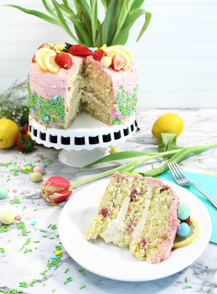 Decorated Strawberry Lemon Cake on cake stand with slice in front.