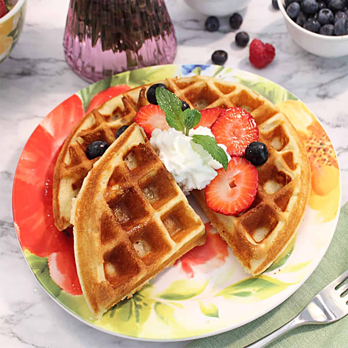 Plated crispy Buttermilk Waffle garnished with fruit and whipped cream.