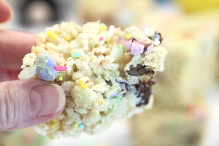 Holding a square of rice krispie treat with bite taken out.
