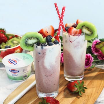Two garnished smoothies on wooden board.